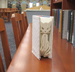 altered book, with pages cut or folded to form an image of a cat on the fore-edge