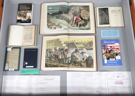 Display case 2: Books on immigration, passenger certificates, and two political cartoons from 1882 and 1903