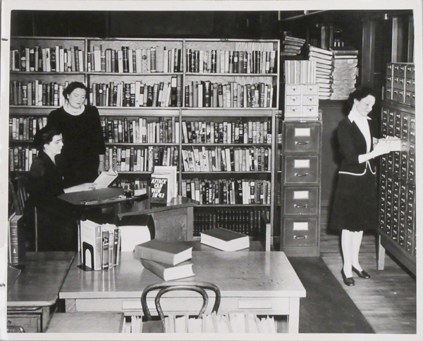 Library office in the 1940s, with two woman looking at a book and on using a card catalog.