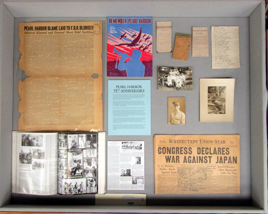 center display case, showing colorful sheet music, a newspaper with a headline about the declaration of war on Japan, and other items commemmorating the Pearl Harbor attack.